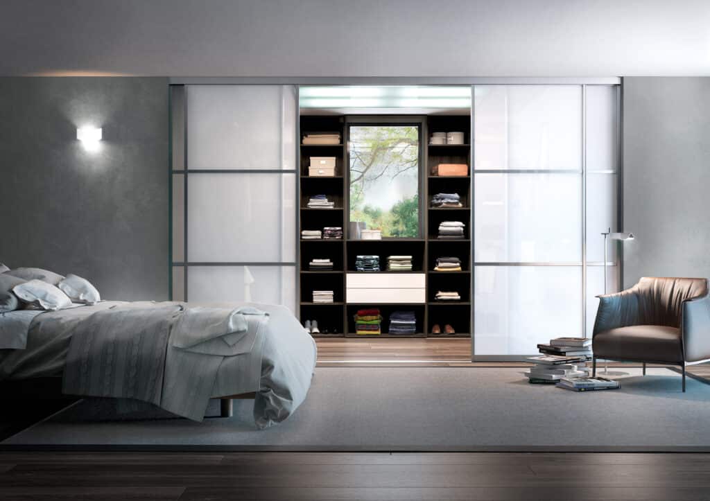 Chambre moderne avec lit, armoire à portes coulissantes blanches, étagères ouvertes avec vêtements, fauteuil en cuir et lampe sur pied.