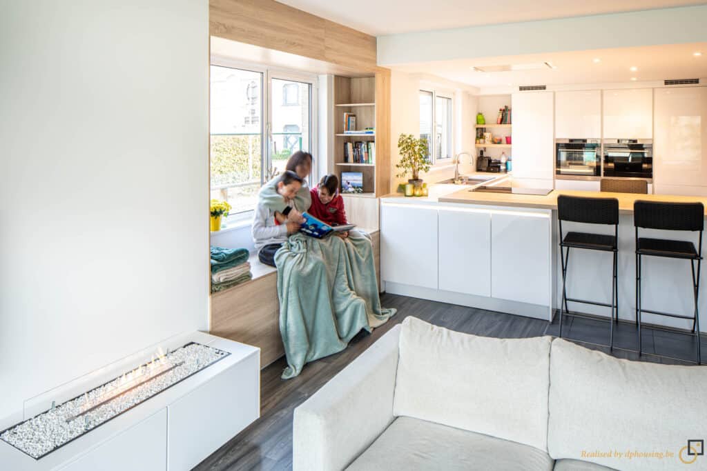 Famille qui lit un livre dans son salon, avec en arrière plan une cuisine blanche aux façades lisses